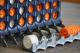 Shown here: Closeup view of base of a dark blue TorKings game unit with a token magazine in the foreground.  The token magazine has upright white tokens on the foreground end and orange tokens in the other end. The tactile stubs that locate the tokens are clearly visible between the token.  The stubs and the magazine make it much easier to track and count your tokens and your winnings.  