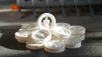 Shown here:  A random pile of white tokens on a grey and tan  grained wooden table top. There is a king token standing upright on the topof the pile - catching the sunlight  that is casting contrasting shadows that highlight the fine detail and interesting shapes of the TorKings breakthrough new 3D sculpted tokens.
